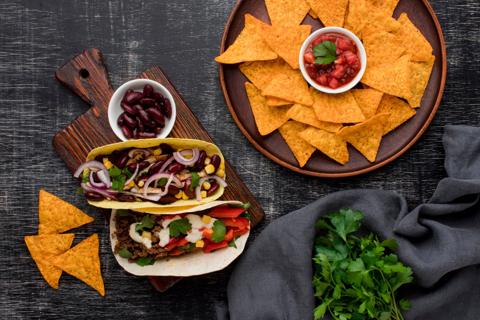 Top view Mexican spread with tacos, nachos, salsa and fresh herbs